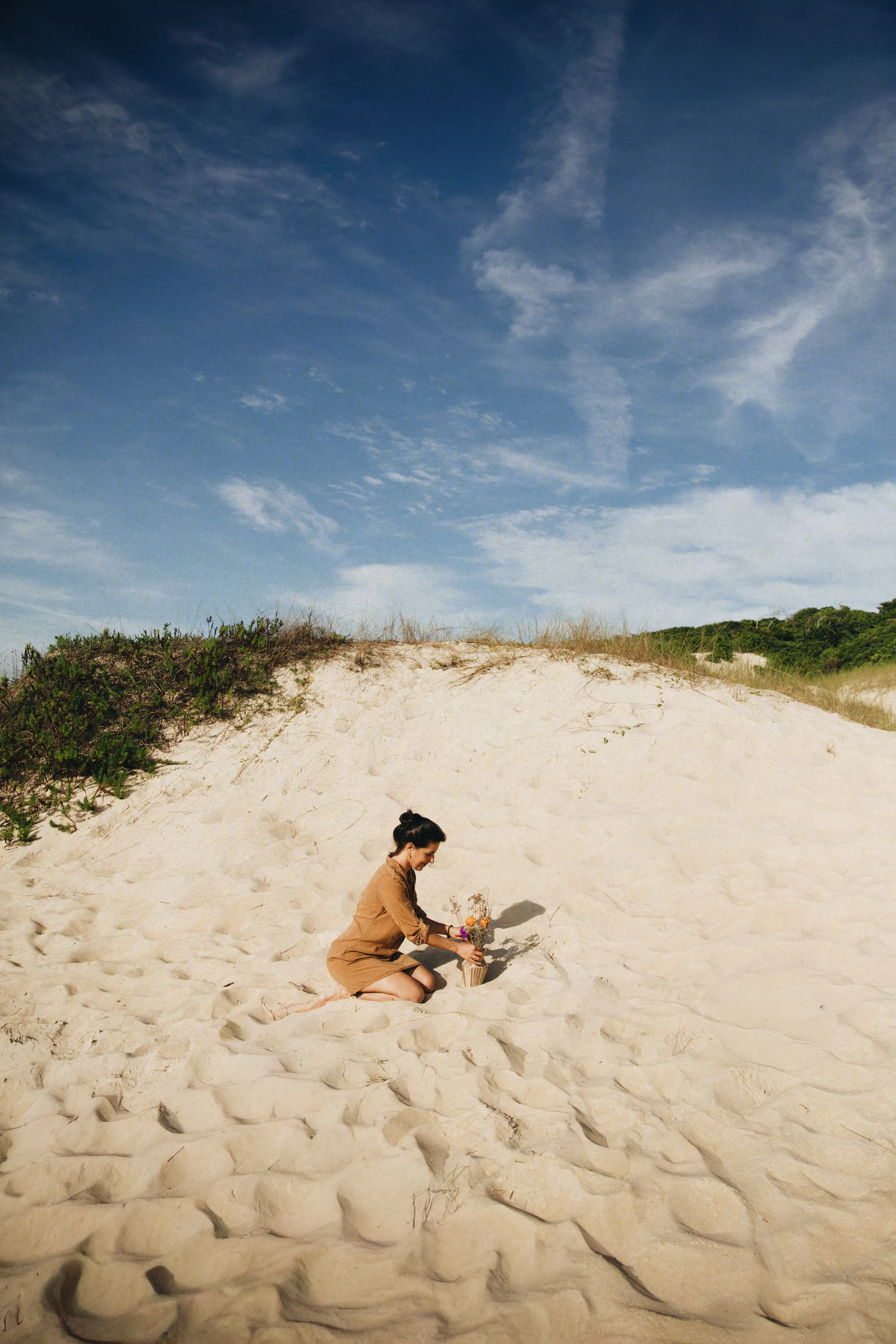 Ramoni kneeling on the dune beside the Dunes #03 vessel with flowers