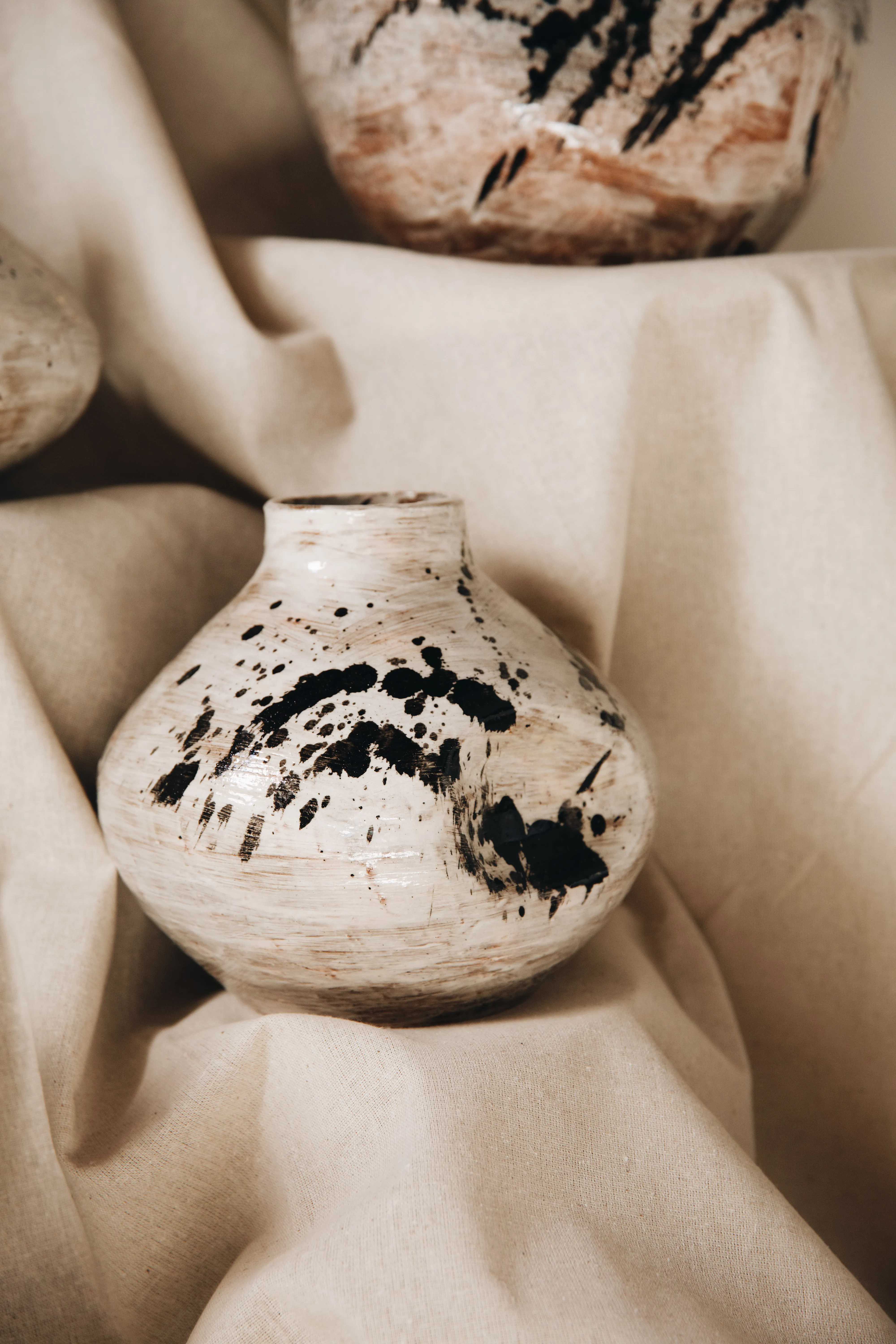 Vaso redondo Gesto #01 sobre tecido bege, esmalte branco com respingos de tinta preta