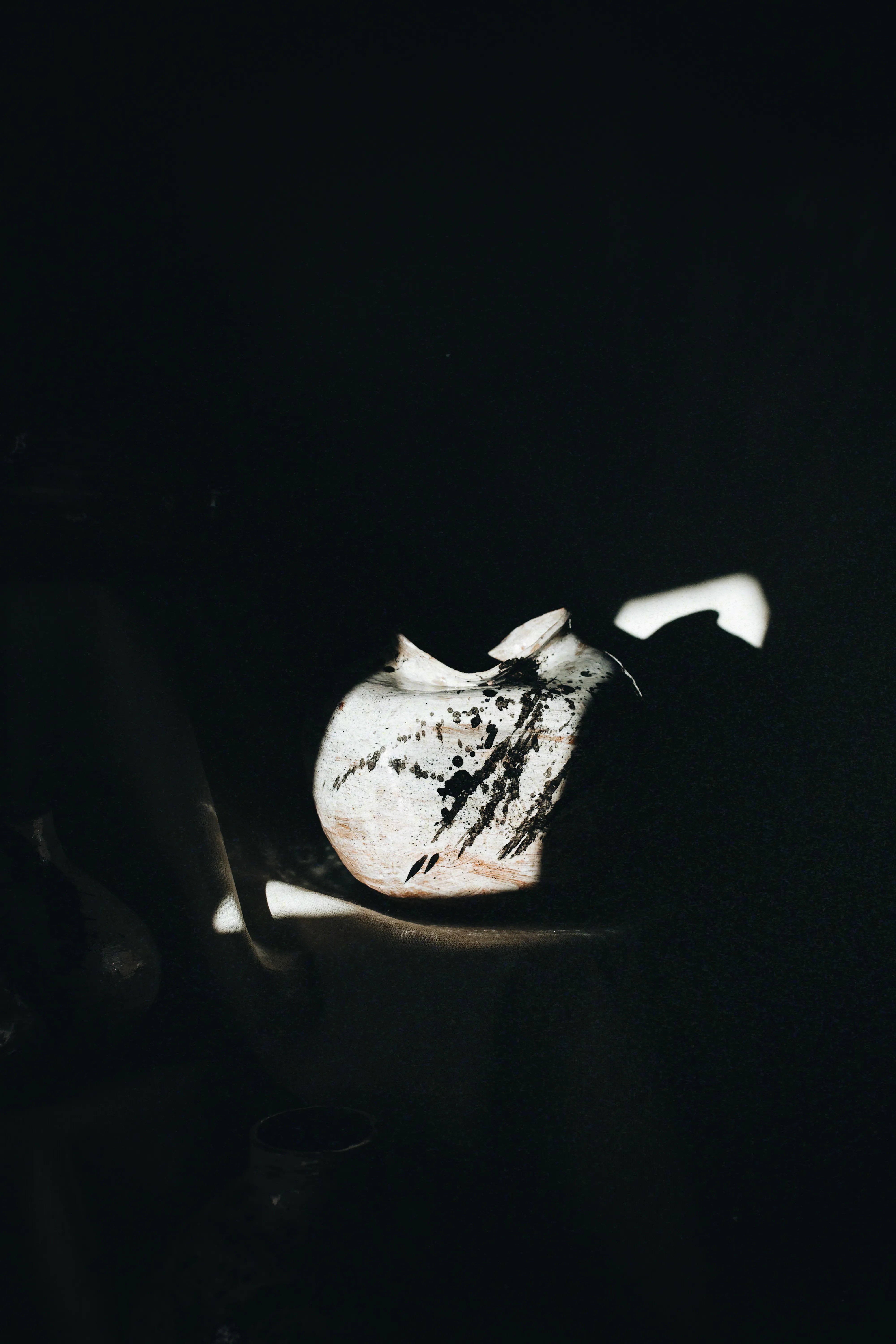 Vaso Gesto #01 em cena escura, iluminado por uma faixa de luz que revela os traços de tinta