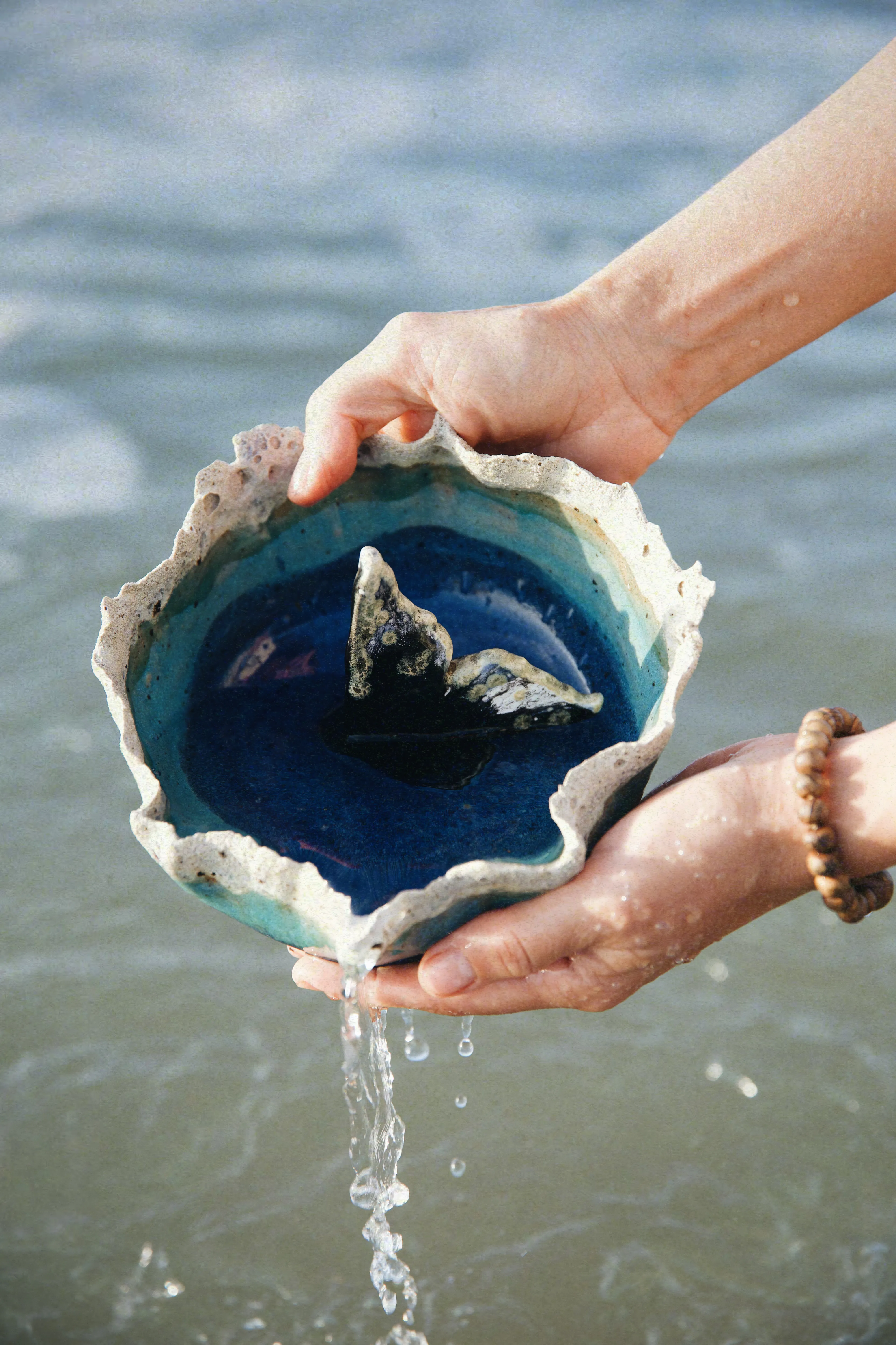 Prato Mar #02 sustentado nas mãos, visto de cima, com a cauda de baleia em azul cobalto