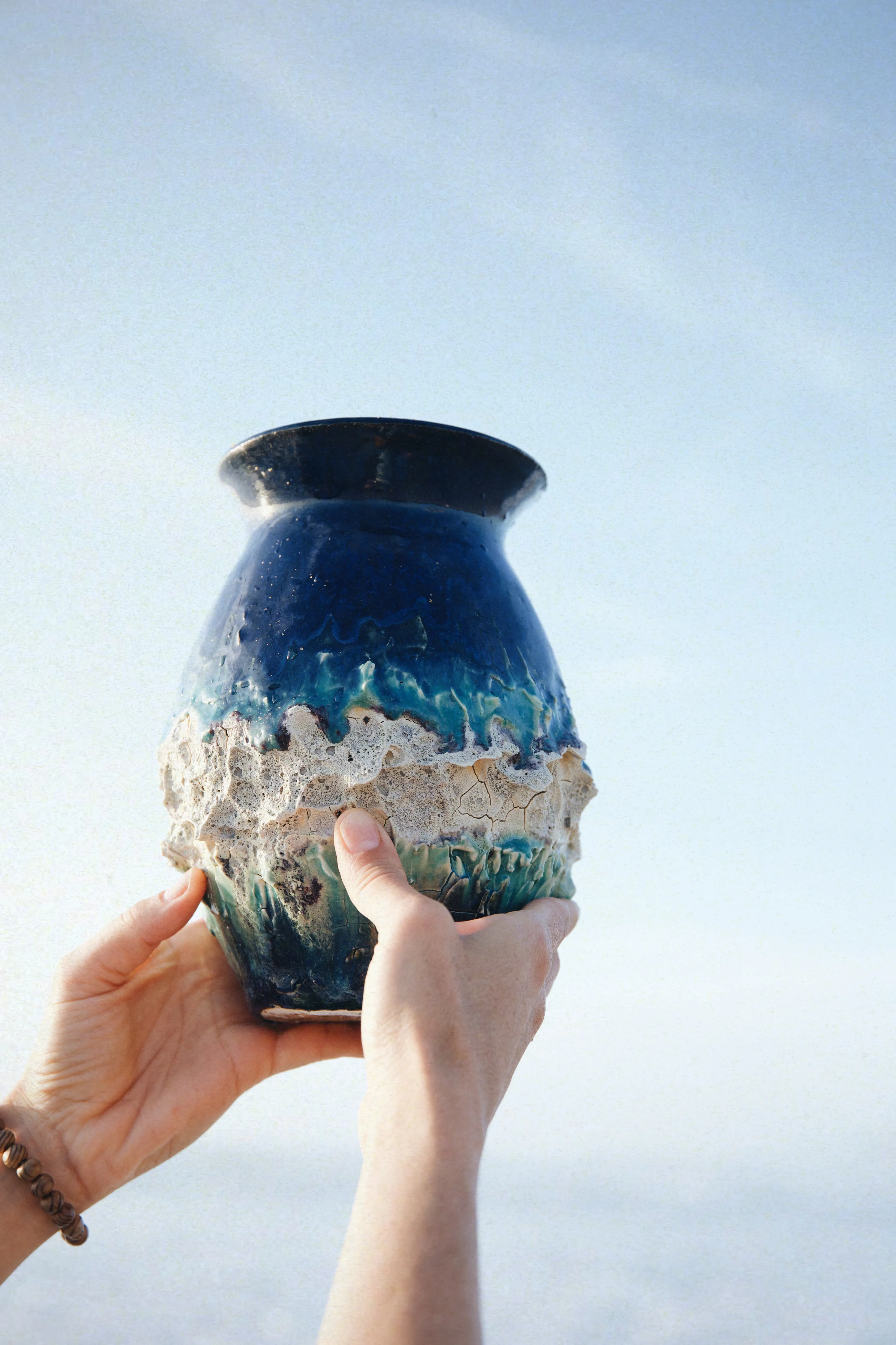 Mãos erguendo o vaso Mar #03 contra o céu