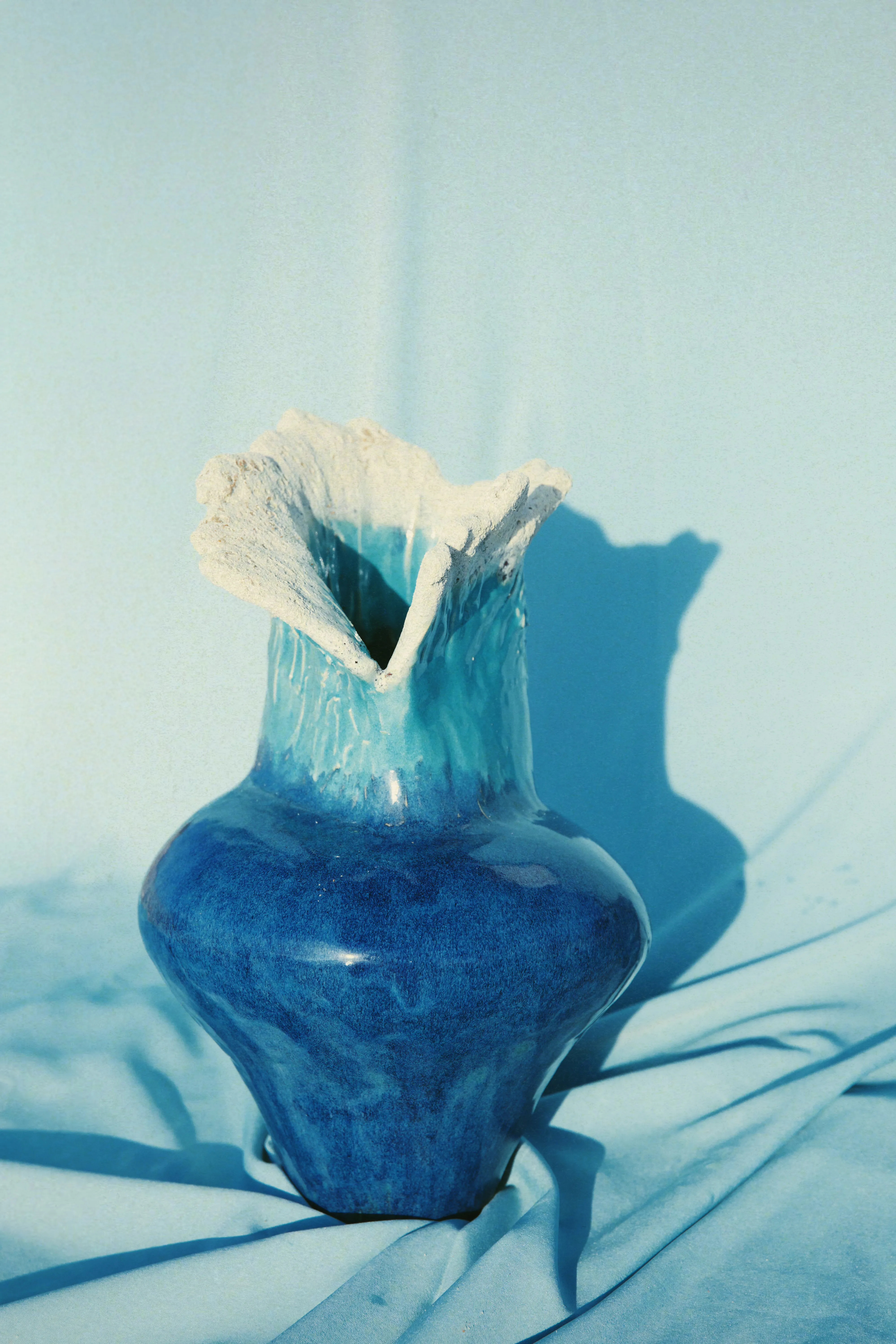 Vaso Mar #04 sobre tecido azul, base estreita e topo largo como uma onda quebrando