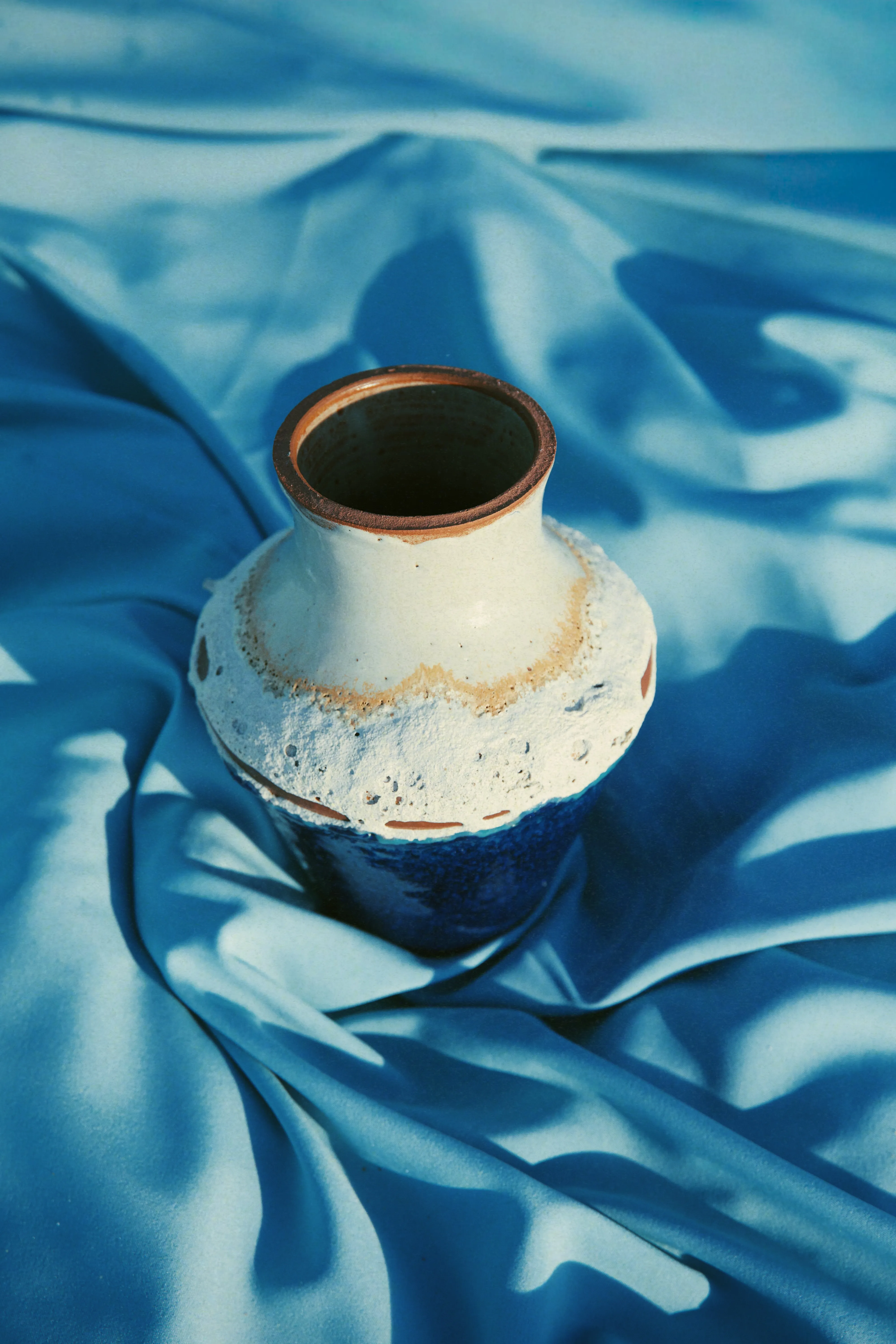 Vaso Mar #05 visto de cima sobre tecido azul, boca com borda de grês exposta